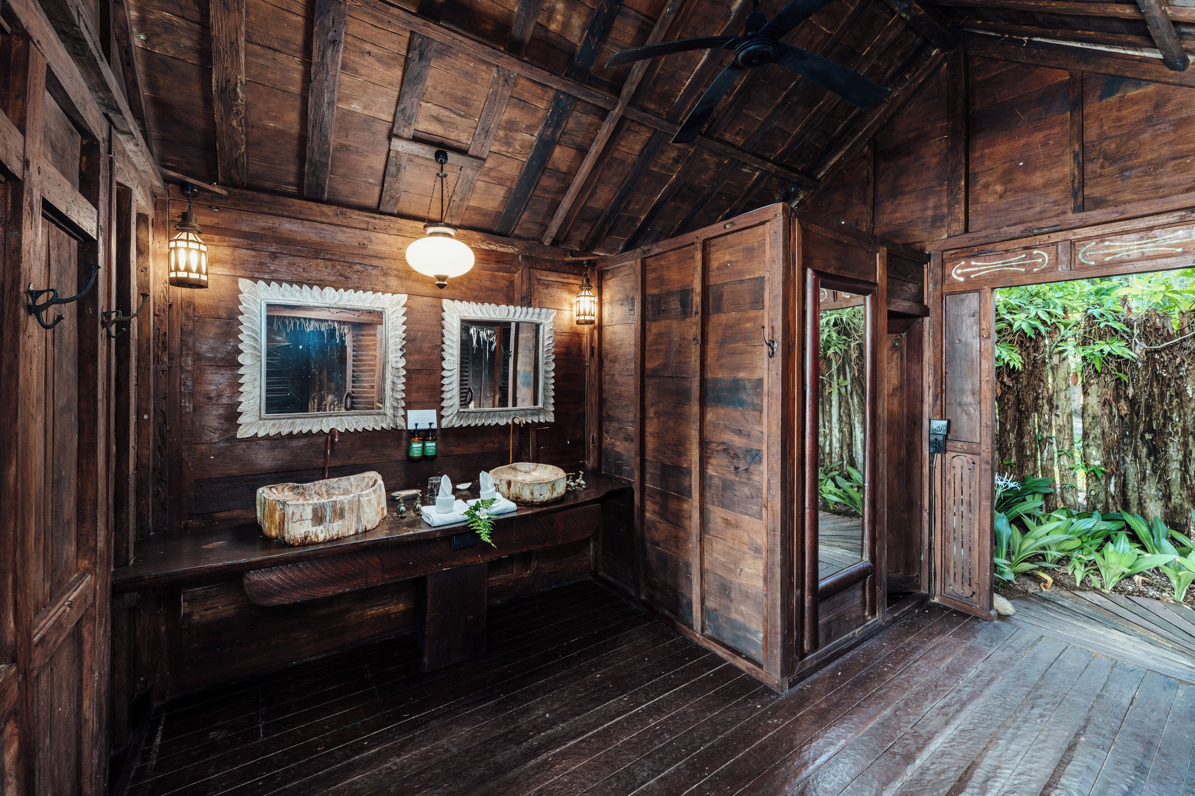 A wooden bathroom with a wooden bench, two mirrors, and a sink.
