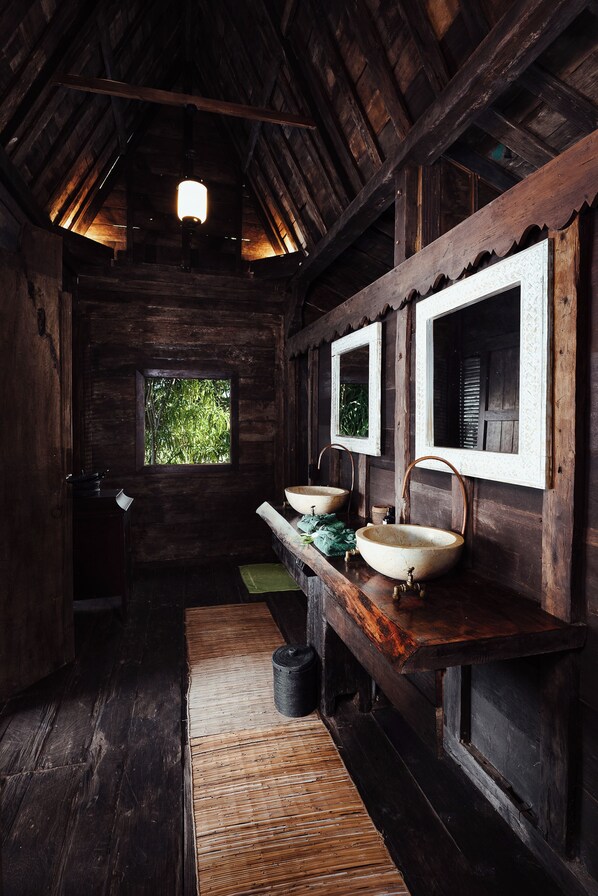 Interior rústico de una cabaña de madera con un ventanal grande, dos lavamanos y piso de madera.
