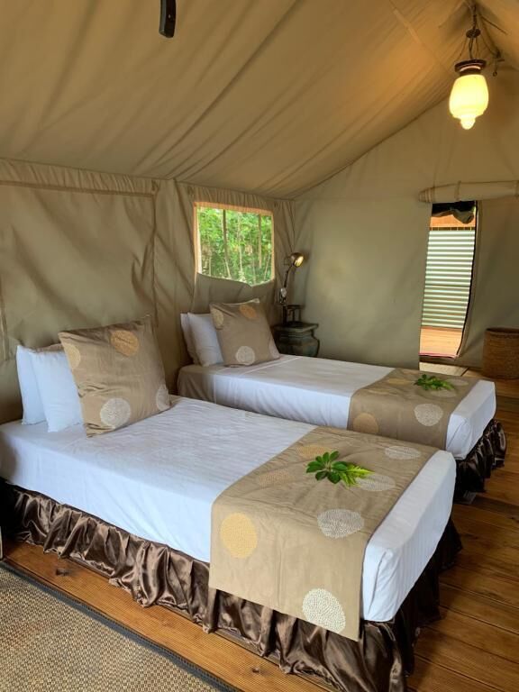 A tented accommodation with two beds, each with a pillow and a bedside lamp.
