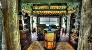 Ein Holzinterieur mit Blick auf das Meer, das einen zentralen Tisch mit einer blauen Vase, Holzkabinetten und ein Regal mit verschiedenen Gegenständen zeigt.