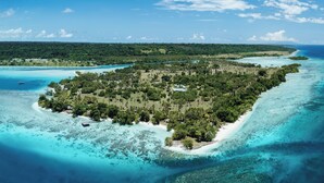 Vista aérea de una isla tropical con aguas turquesas cristalinas, abundante vegetación y algunos edificios.