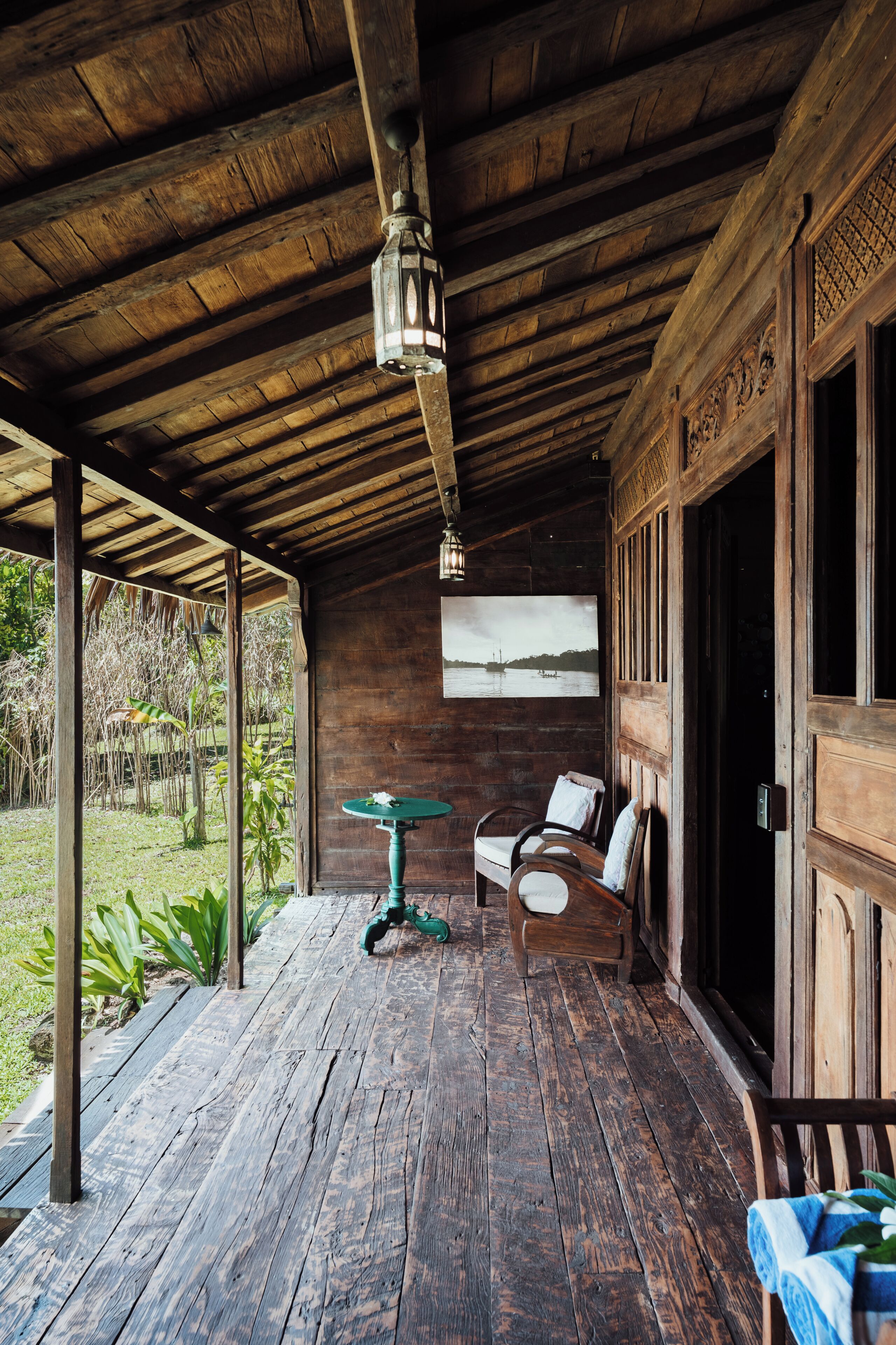 A wooden porch with a table and chairs, a hanging lantern, and a framed picture on the wall.