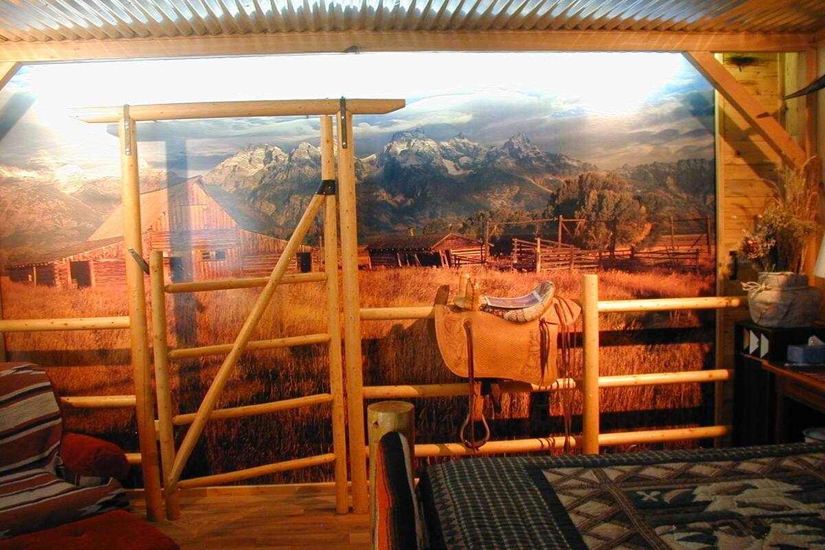 Quarto rústico com escada de madeira, sela e grande janela com vista para as montanhas.