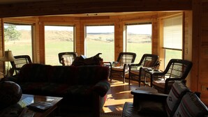 Un interior de madera con un sofá, sillas y una mesa. Amplias ventanas ofrecen vistas al exterior.