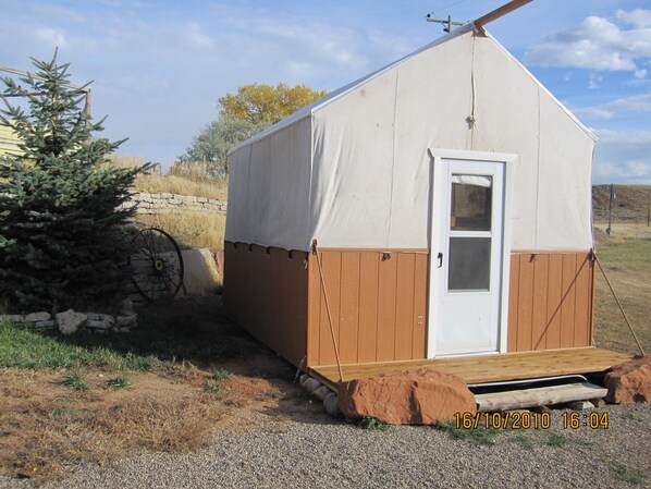 A small, single-story cabin with a white door and brown siding, situated on a gravel ground with a wooden ramp leading up to the entrance. - K3 Guest Ranch Bed & Breakfast (Cody)
