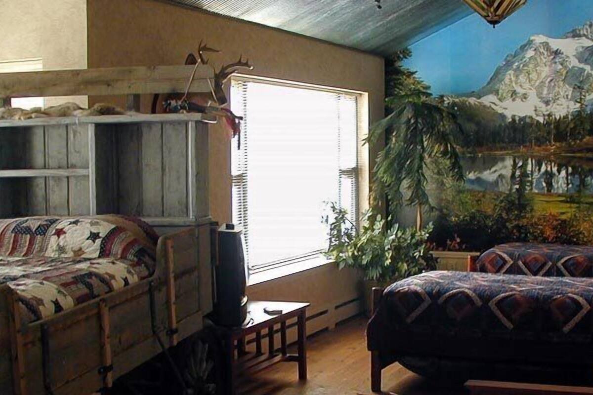 Quarto com cama, escrivaninha, cadeira e um mural de paisagem montanhosa.