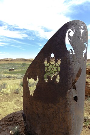 A metal sculpture with animal and human figures, set against a rural landscape with a clear sky.