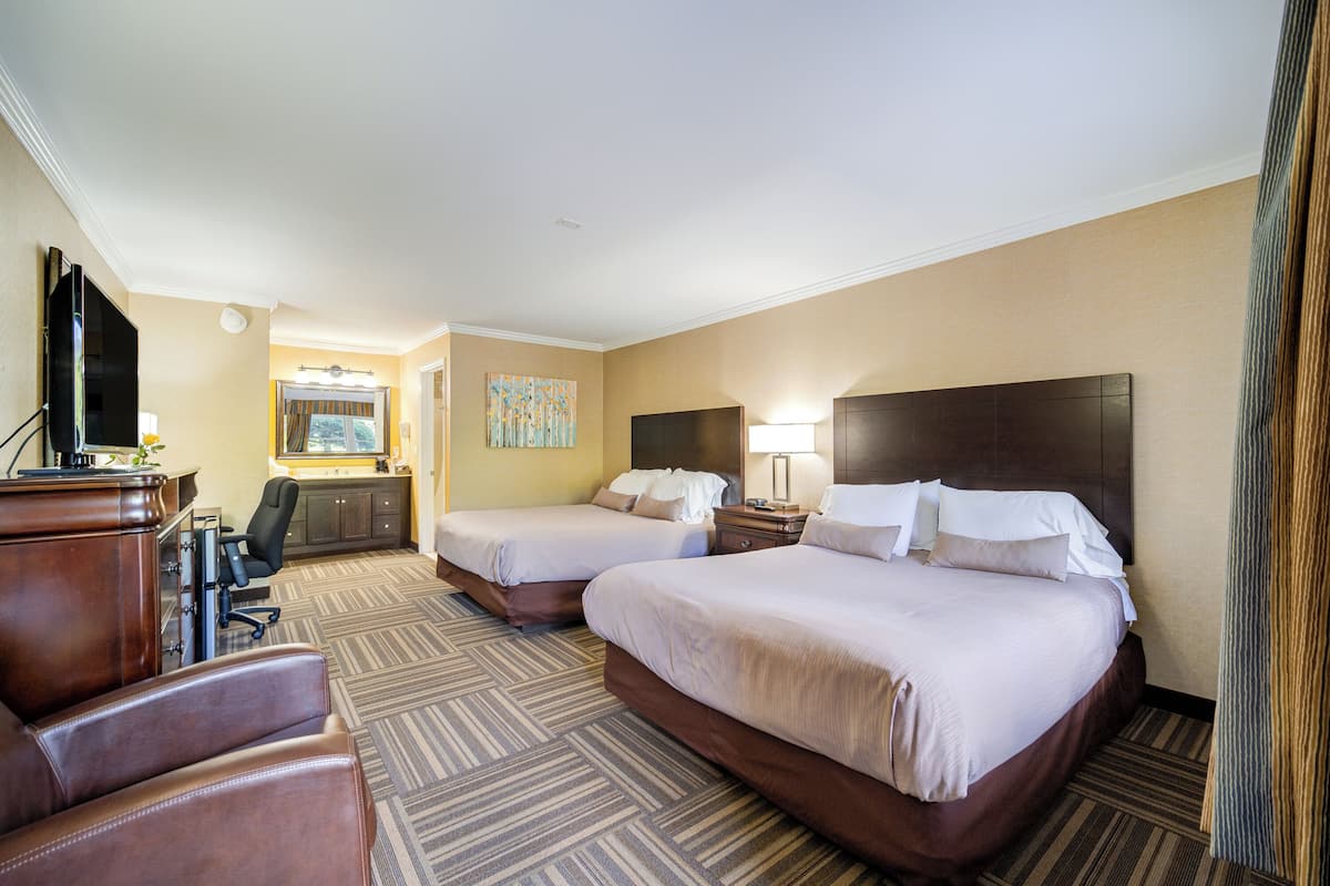 A hotel room with two beds, a desk, a chair, and a TV.