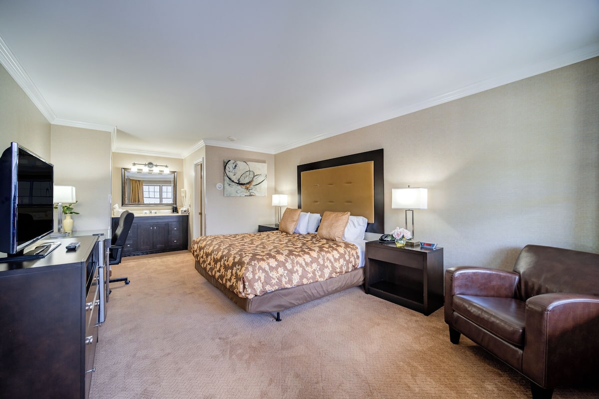 A hotel room with a large bed, a desk with a computer, a chair, and a couch.