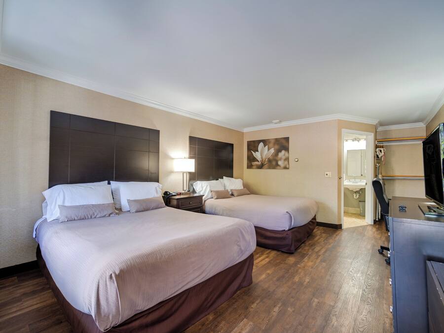 Een hotelkamer met twee bedden, een bureau, een televisie en een badkamer, zichtbaar door een geopende deur.