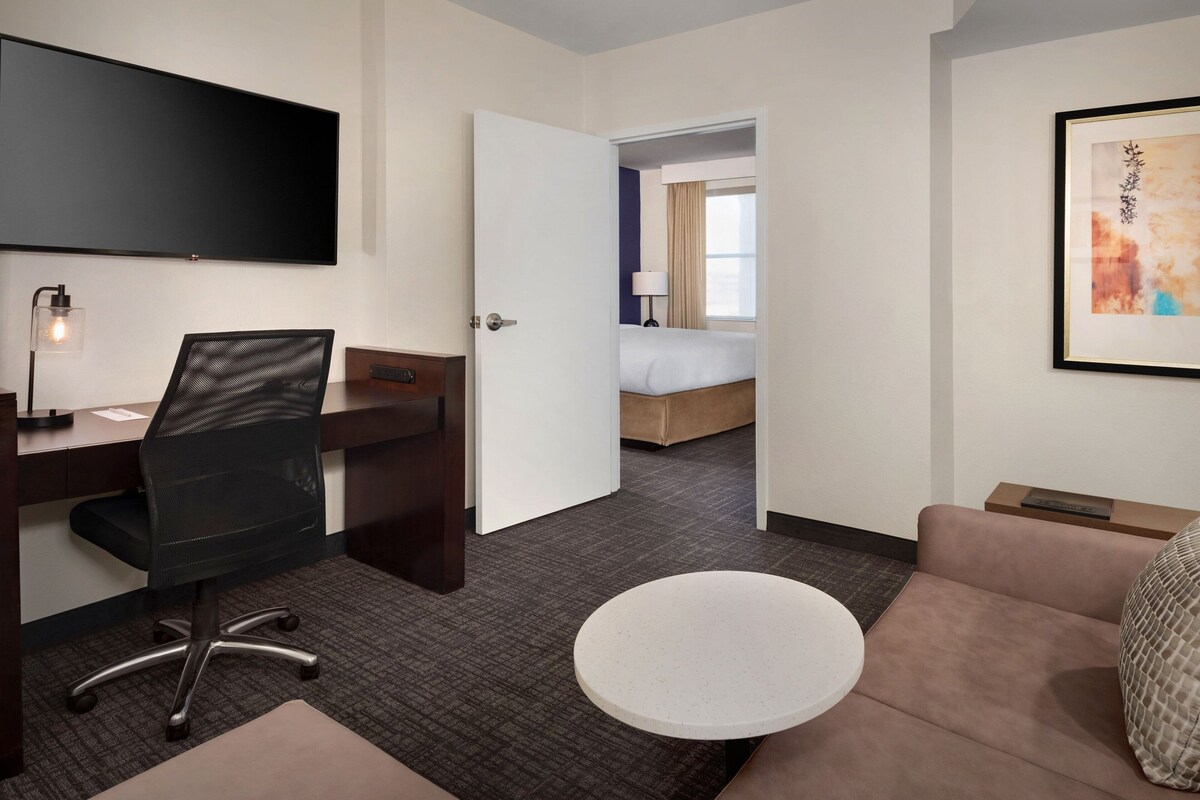 A hotel room with a desk, chair, round table, sofa, and a bed in the background.