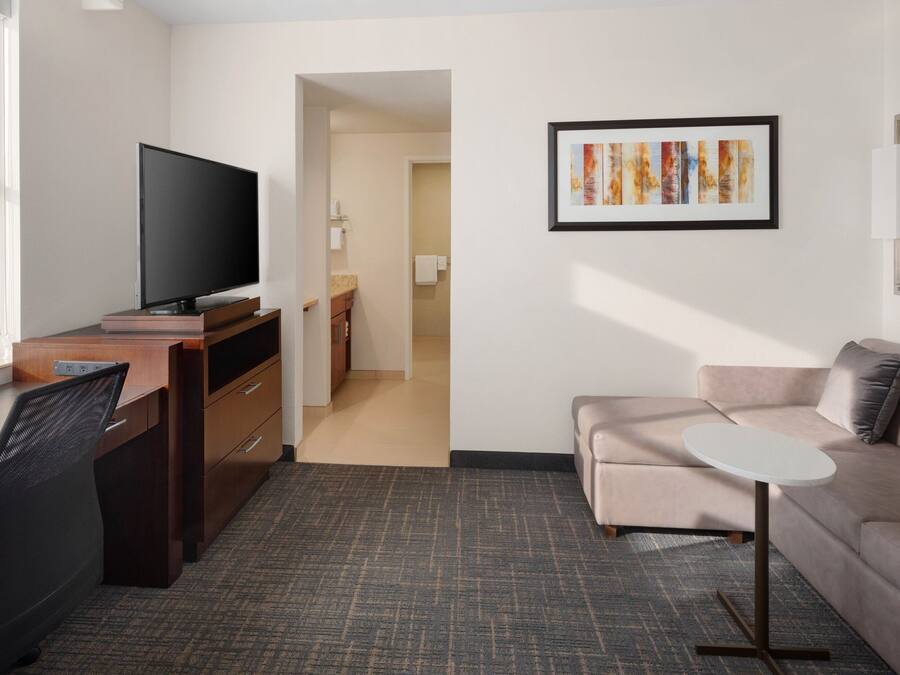 Una habitación de hotel moderna con televisión de pantalla plana, escritorio, sofá y una pequeña mesa redonda.