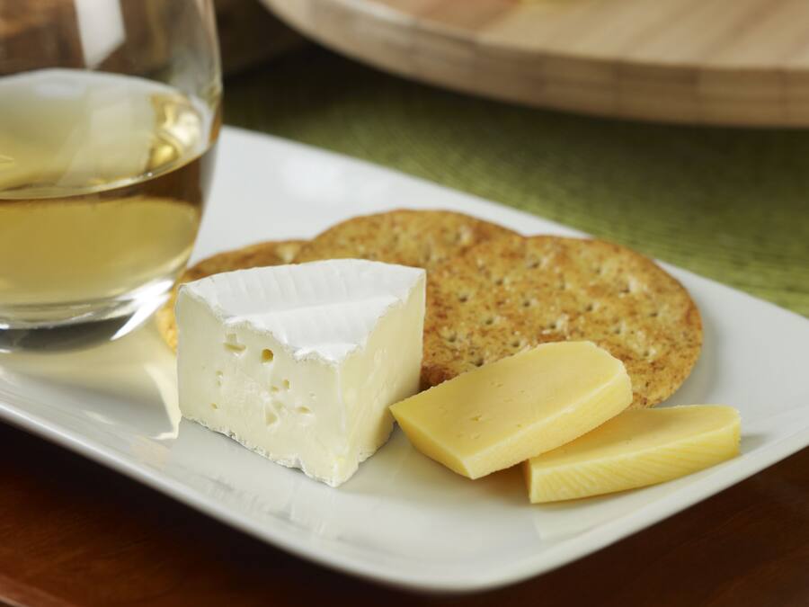 A plate with cheese, crackers, and a glass of white wine on a table.