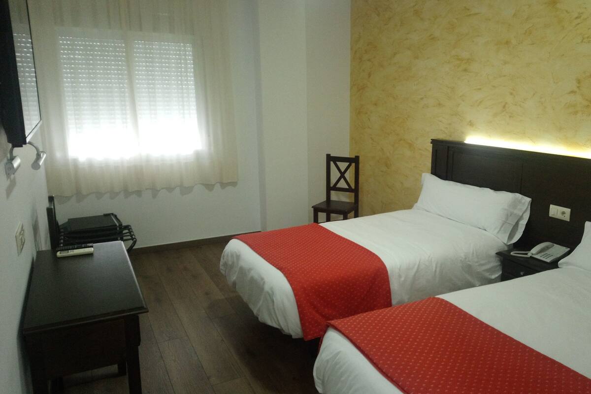 Habitación de hotel con dos camas, un escritorio, una silla y un teléfono.