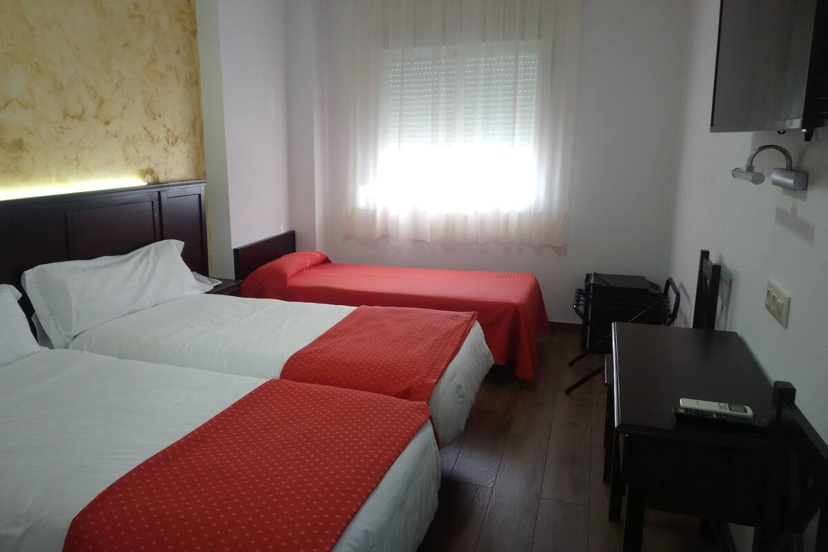 Habitación de hotel con dos camas, un escritorio, una silla, un televisor y una ventana con cortinas.