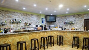 Een bar met een stenen muur, een flatscreen televisie boven de toonbank en verschillende barkrukken.