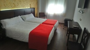 Een hotelkamer met twee bedden, een bureau, een stoel en een televisie aan de muur.