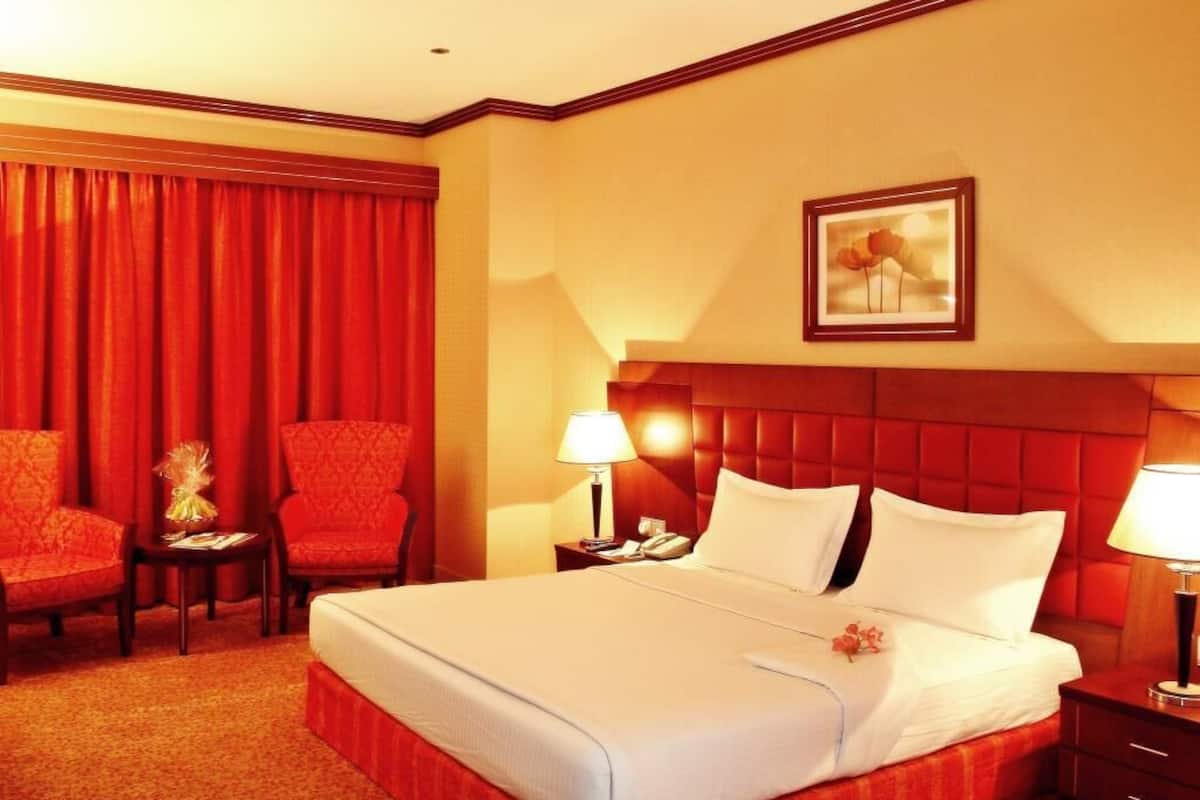 Une chambre d’hôtel avec un grand lit, deux chaises, une table de chevet avec une lampe et un tableau encadré au mur.