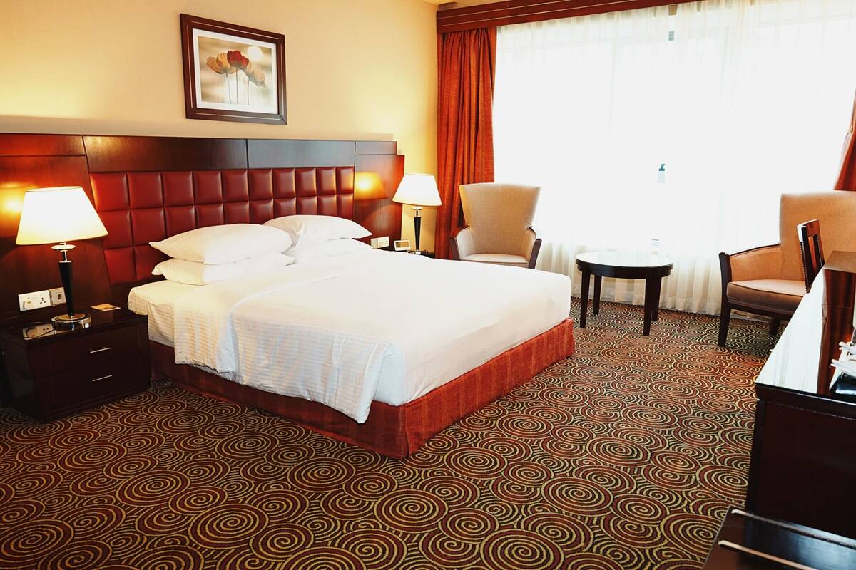 Une chambre d’hôtel avec un grand lit, deux chaises, une petite table et une table de chevet avec des lampes.