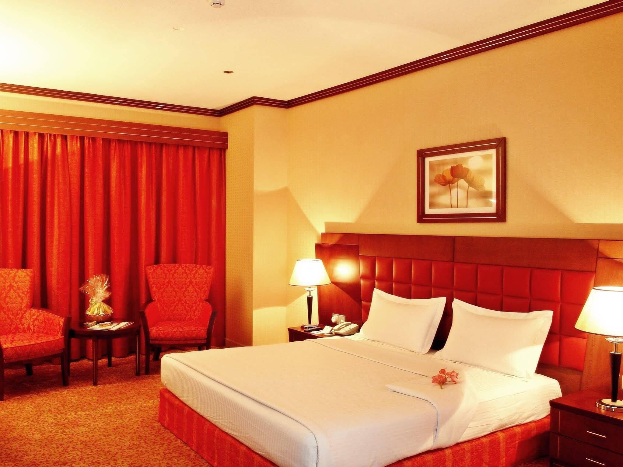 A hotel room with a large bed, two chairs, a nightstand with a lamp, and a painting on the wall.