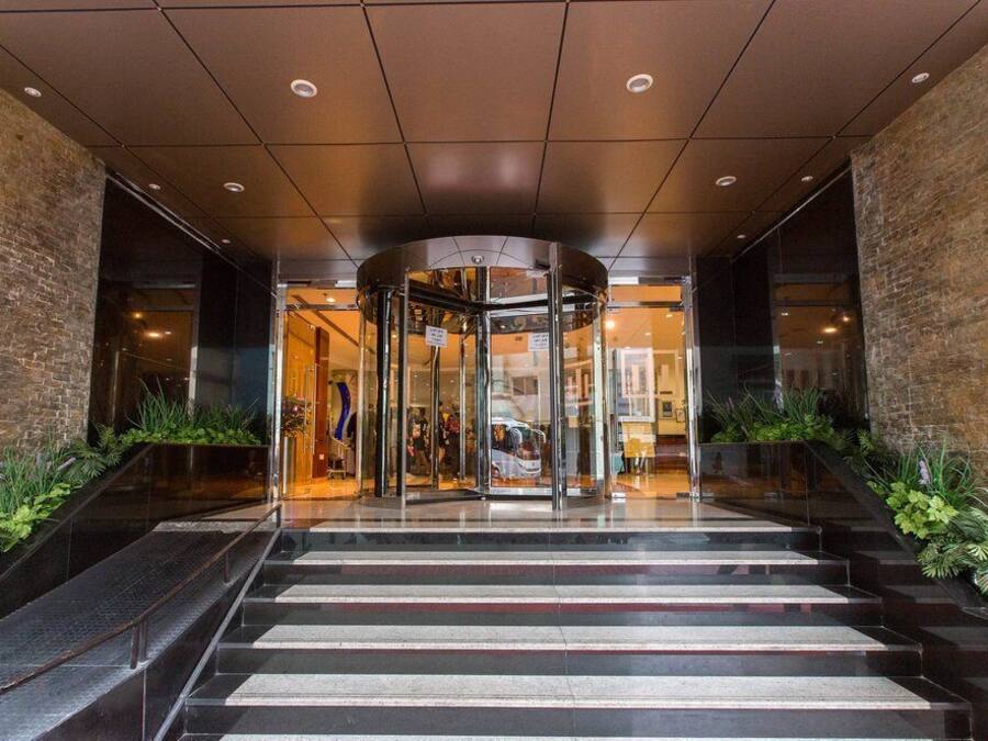 Entrada de hotel com porta giratória, escada e paredes de tijolo.
