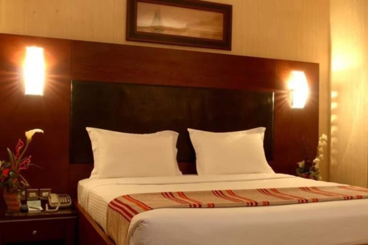 Une chambre d’hôtel avec un grand lit, deux lampes de chevet, une table de chevet avec un téléphone et un tableau encadré au mur.