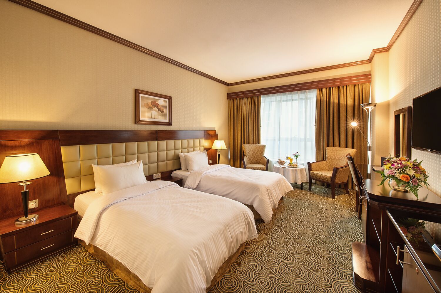 A hotel room with two beds, a desk, a chair, a TV, and a window with curtains.