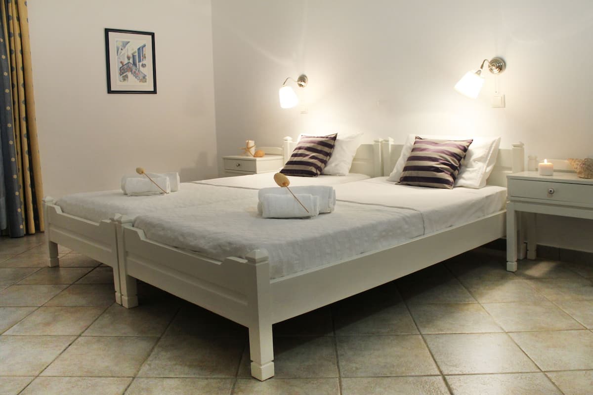 Un lit double avec une literie blanche, deux tables de chevet avec des lampes, une petite table de nuit avec une bougie et un tableau encadré au mur.