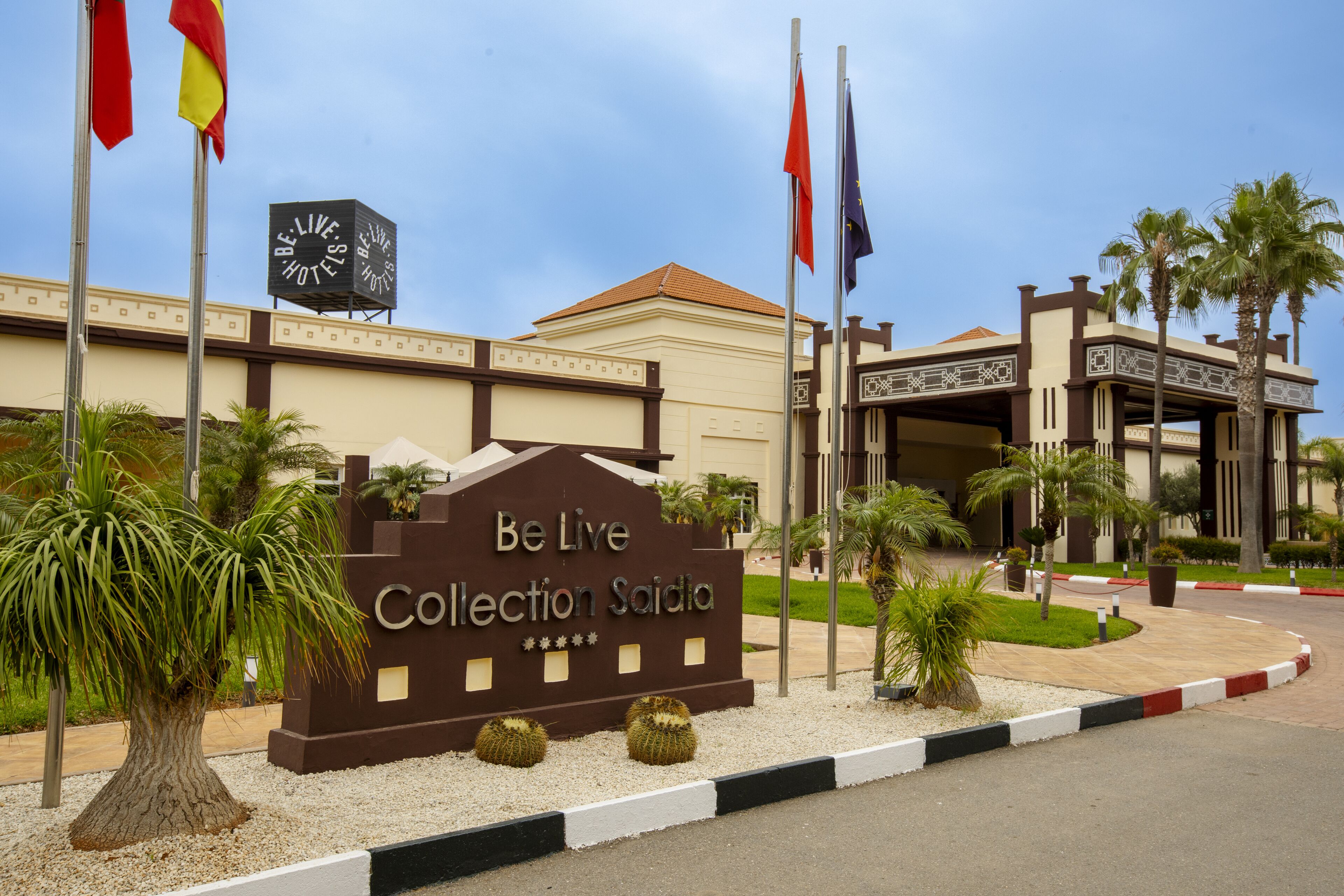 L’entrée d’un hôtel, avec une enseigne indiquant « Be Live Collection Saidia », des palmiers et des drapeaux.
