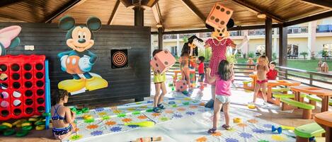 A covered outdoor play area with a Mickey Mouse mural, colorful play mats, and various play structures.