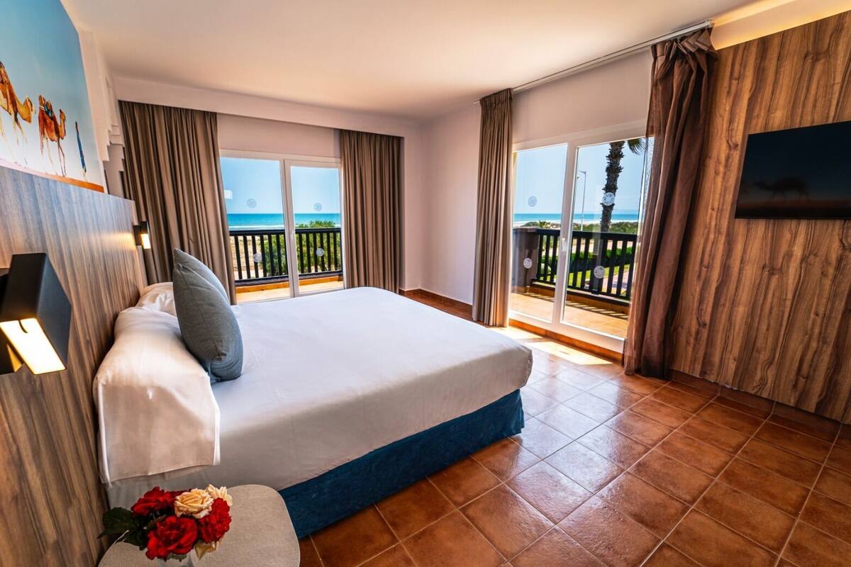 Habitación de hotel con una cama grande, un balcón con vistas al mar y un televisor de pantalla plana en la pared.