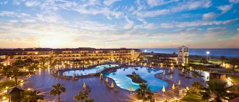 Un resort con una piscina amplia, palmeras y una torre.