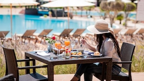 Una mesa de comedor con comida, una piscina y sillones de descanso al fondo.