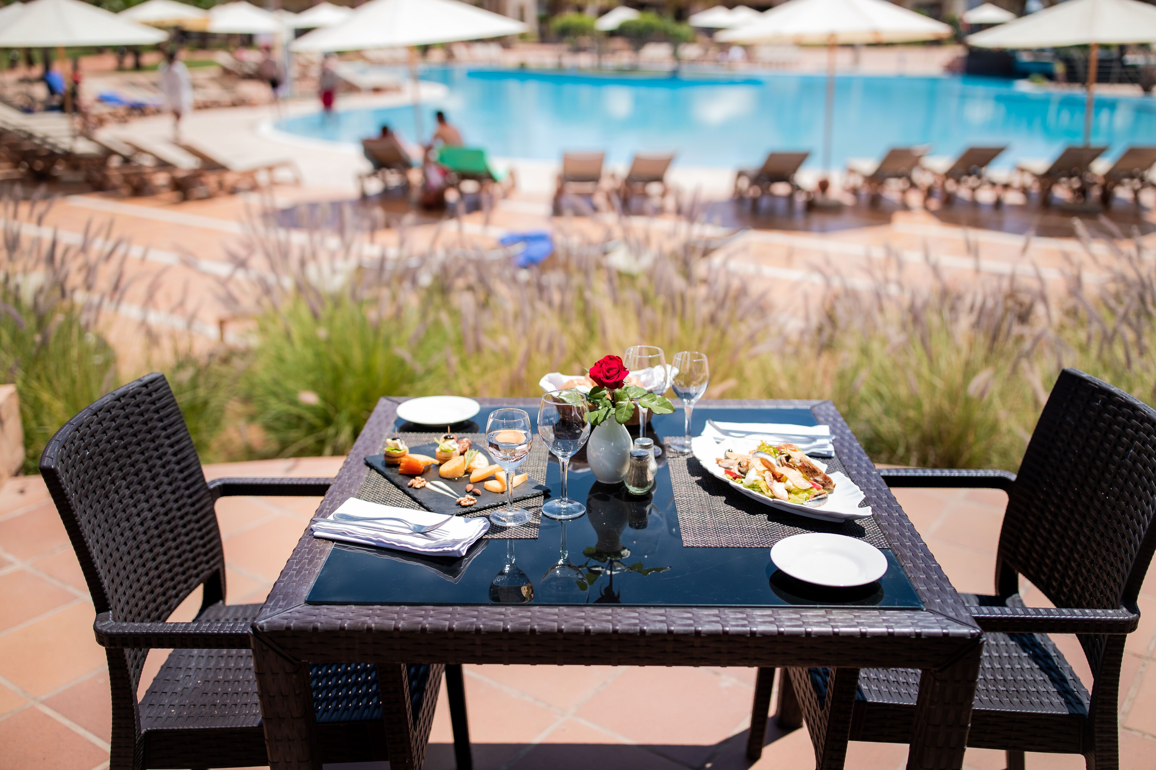 Mesa de comedor al aire libre con vista a una piscina y sillones de descanso.