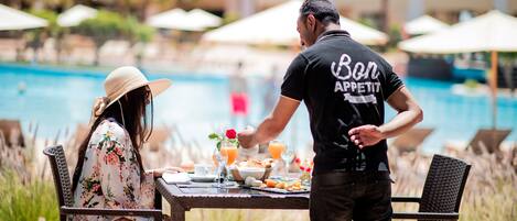A dining table with breakfast items and a pool in the background.
