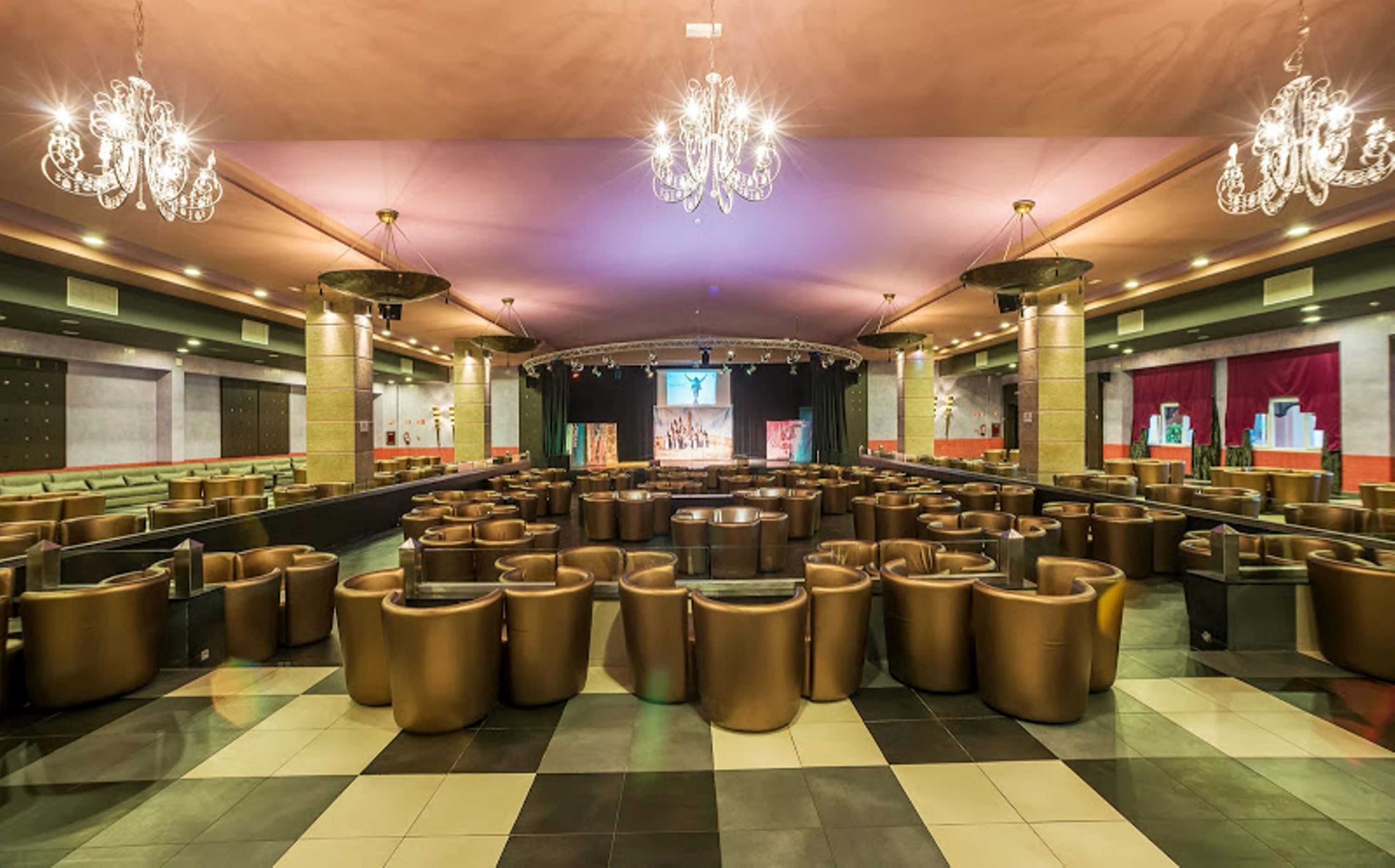 A spacious lobby with a checkered floor, multiple seating areas, and a stage at the far end.
