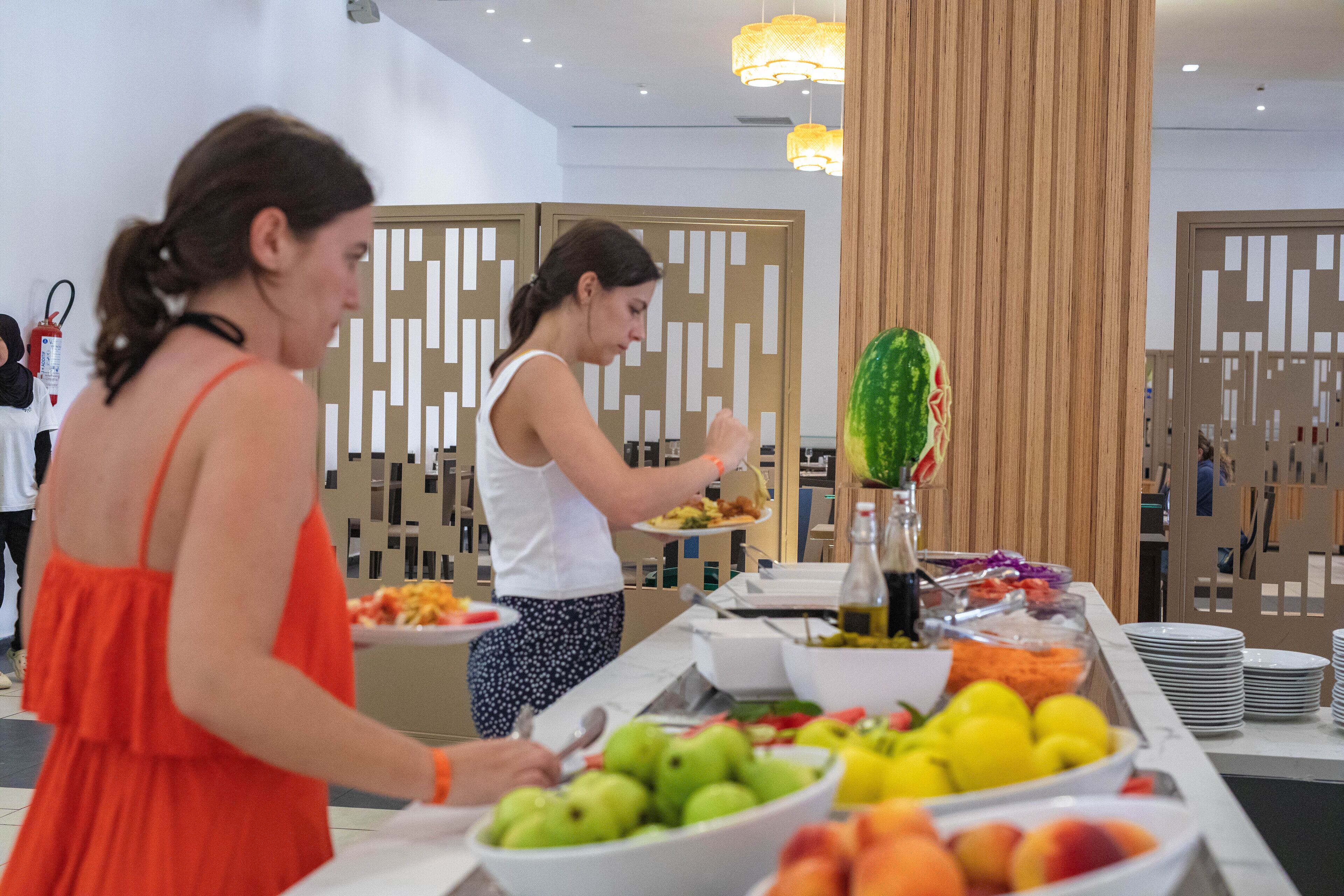 Un espace buffet proposant une variété de fruits et de légumes, un distributeur d’eau et un mur décoratif en arrière-plan.