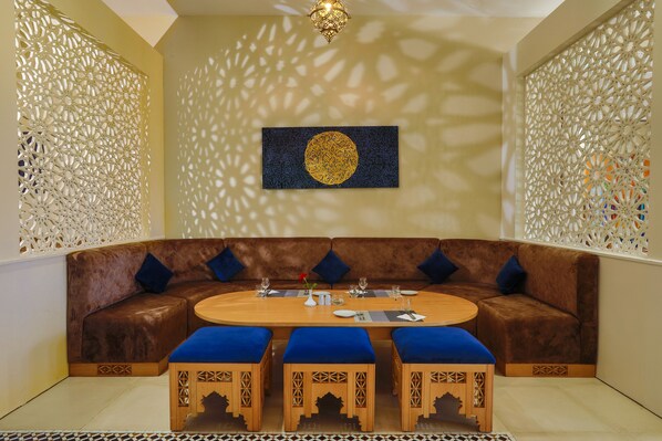 Un rincón acogedor con un sofá marrón y cojines azules, una mesa de madera con un florero, y paneles decorativos con diseños elaborados.