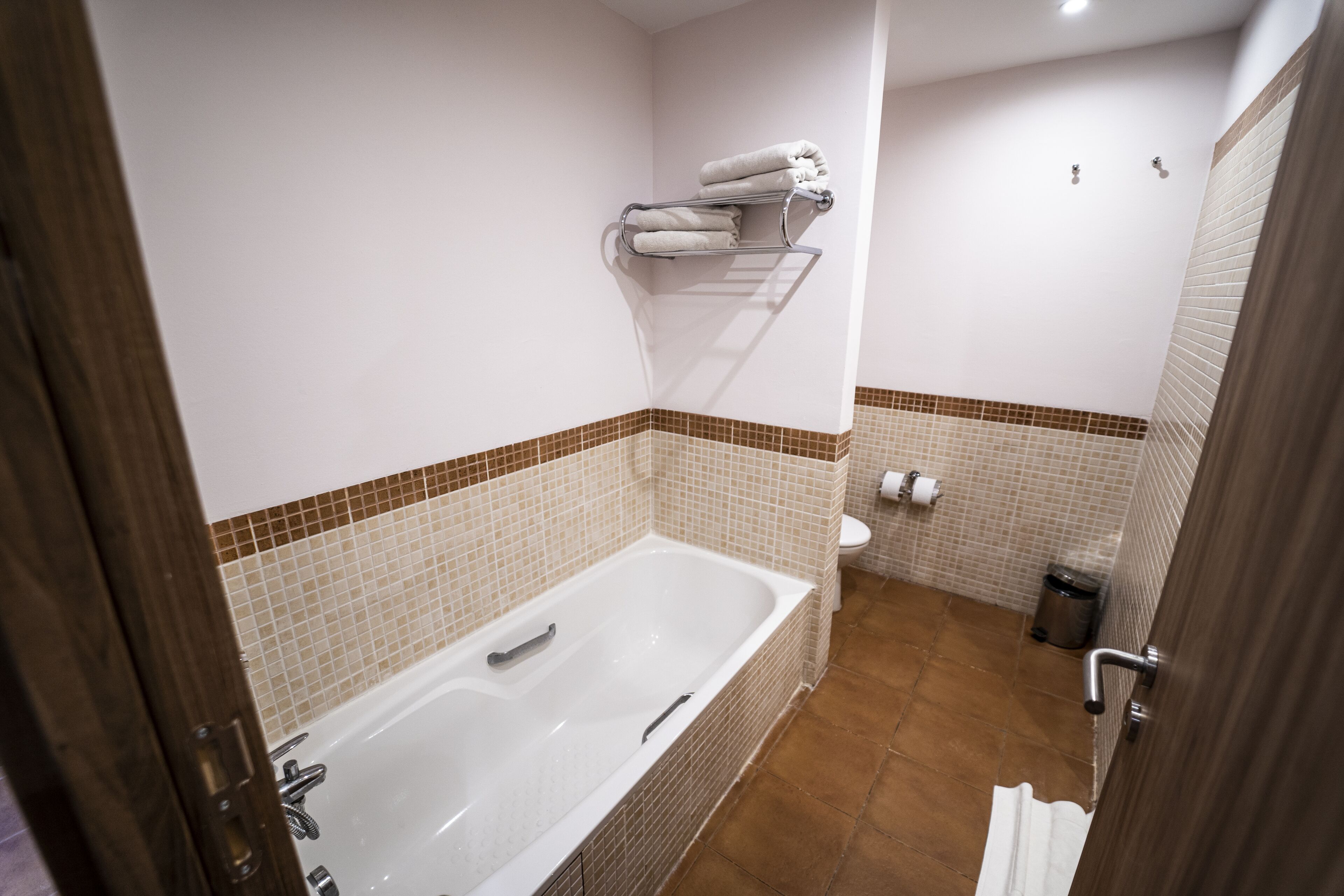 A bathroom with a bathtub, a towel rack, a toilet, and a trash can.