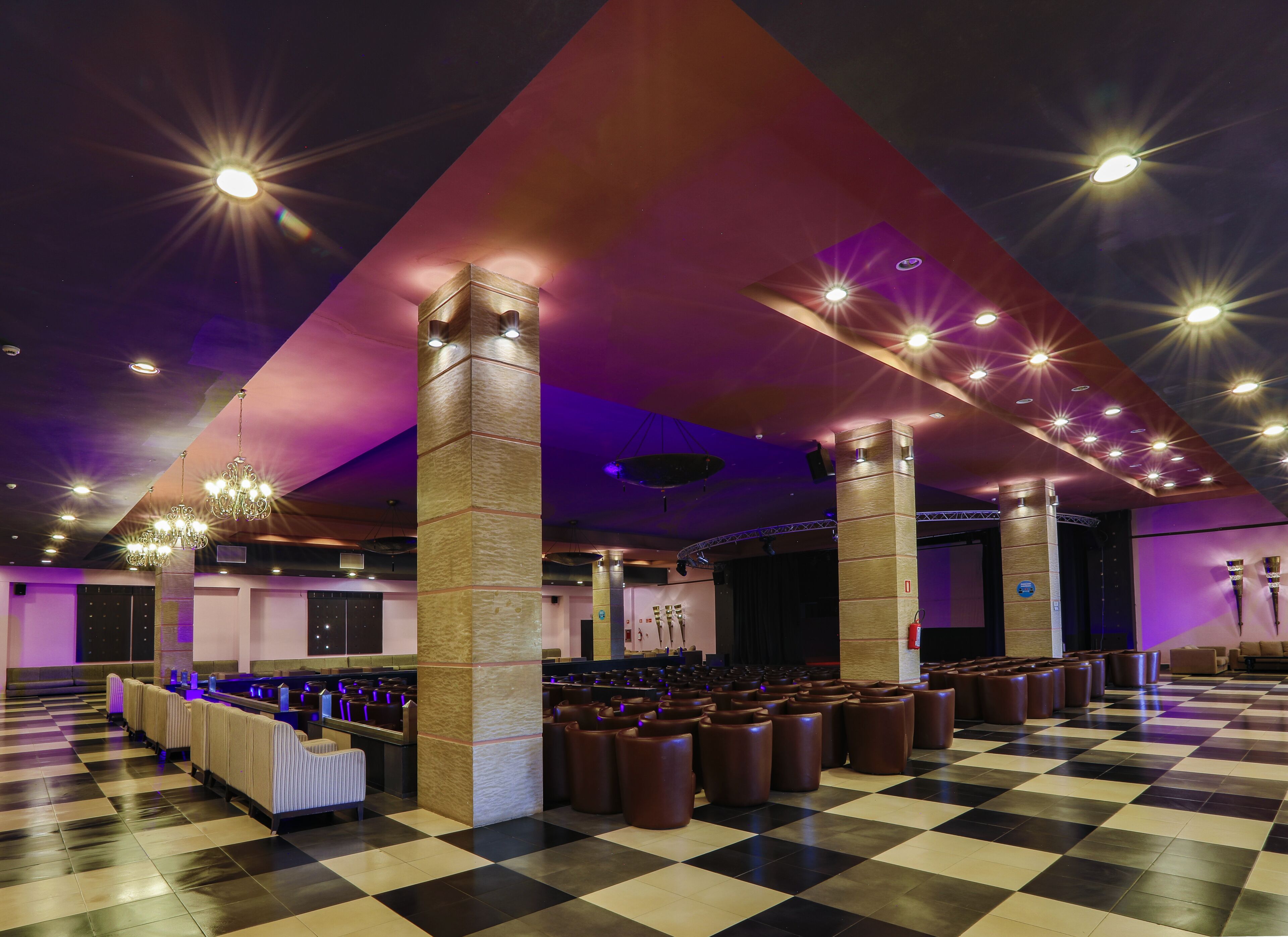 Un amplio hall de hotel con suelo de cuadros, varias zonas de estar y un escenario con iluminación.