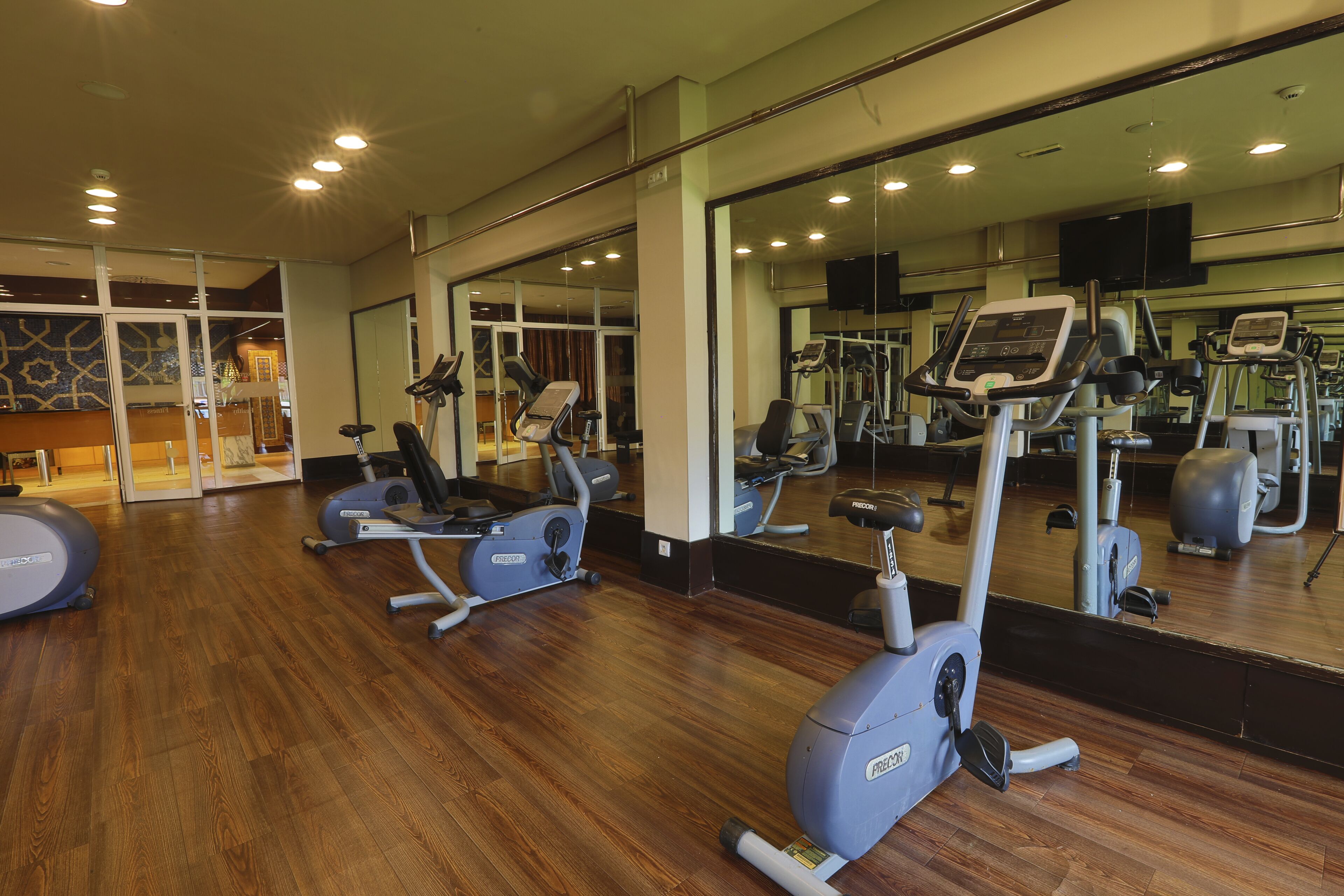 Academia com máquinas de cardio, espelhos e piso de madeira.