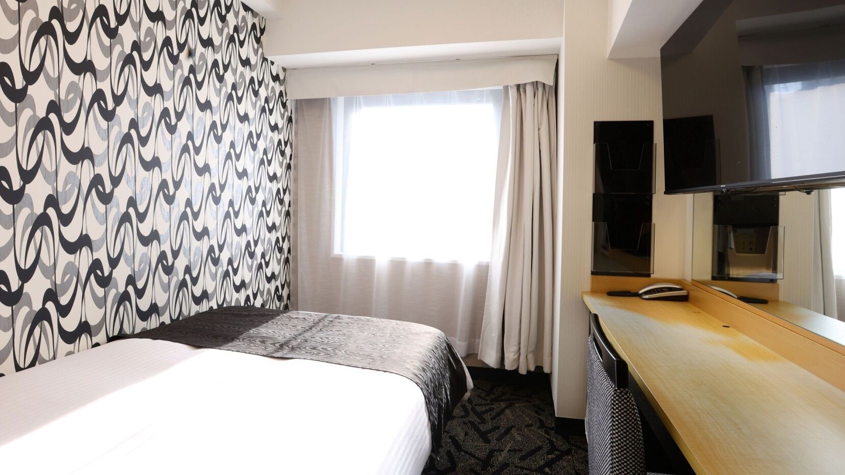 A hotel room with a bed, a desk, a television, and a window with curtains.