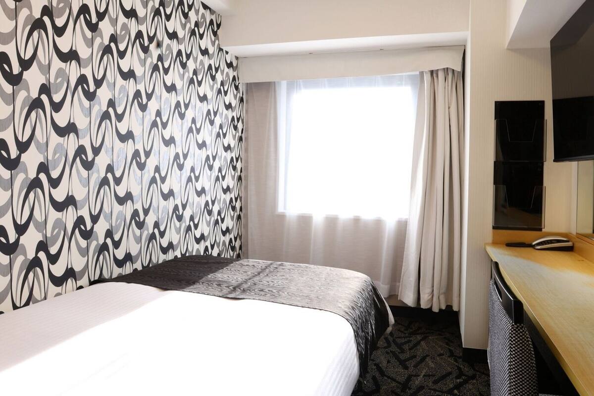 A hotel room with a bed, a desk, a television, and a window with curtains.