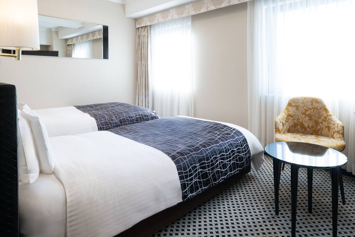 A hotel room with a double bed, a small round table, a chair, and a large mirror on the wall.