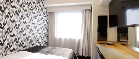 A hotel room with a bed, a desk, a television, and a window with curtains.