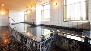 A stone-floored indoor pool area with tiled walls and large windows.