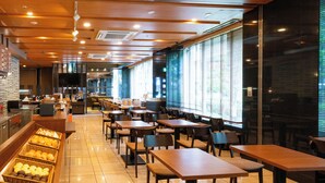 A spacious cafe with wooden tables and chairs, a counter with fruit baskets, and large windows providing natural light.