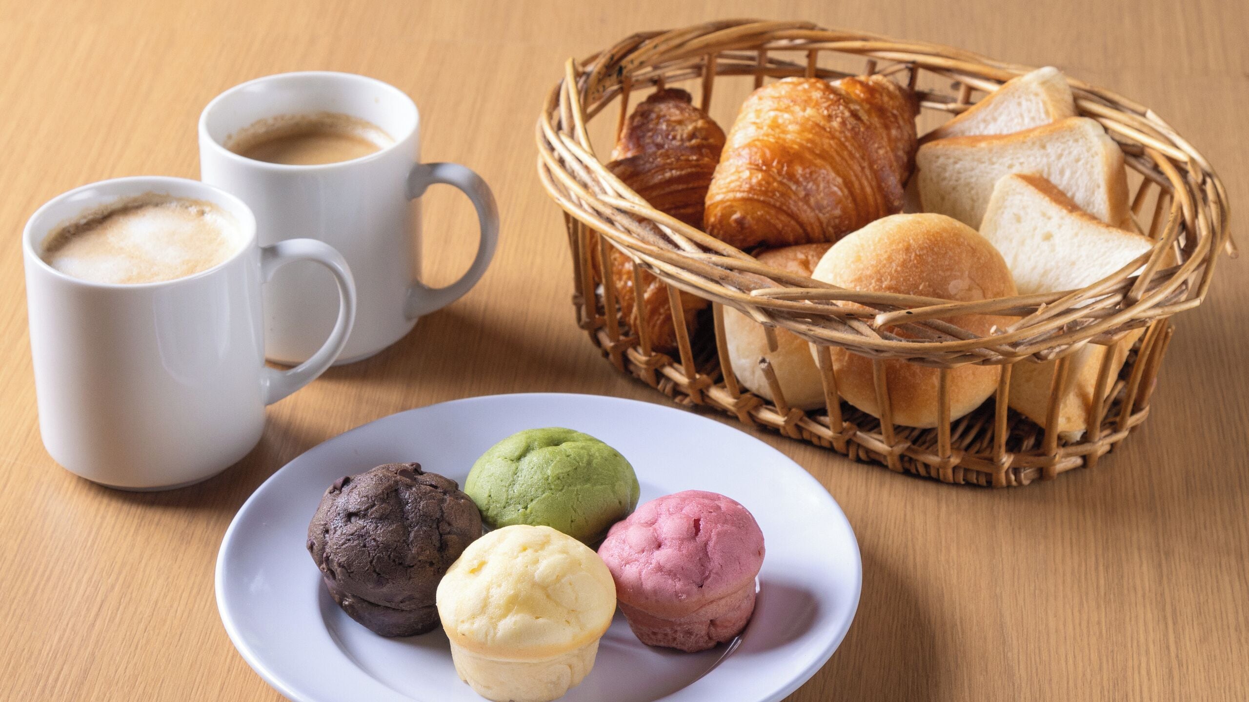 Ein Tisch mit einer Platte bunter Gebäckstücke, einem Brotkorb und zwei Kaffeetassen.