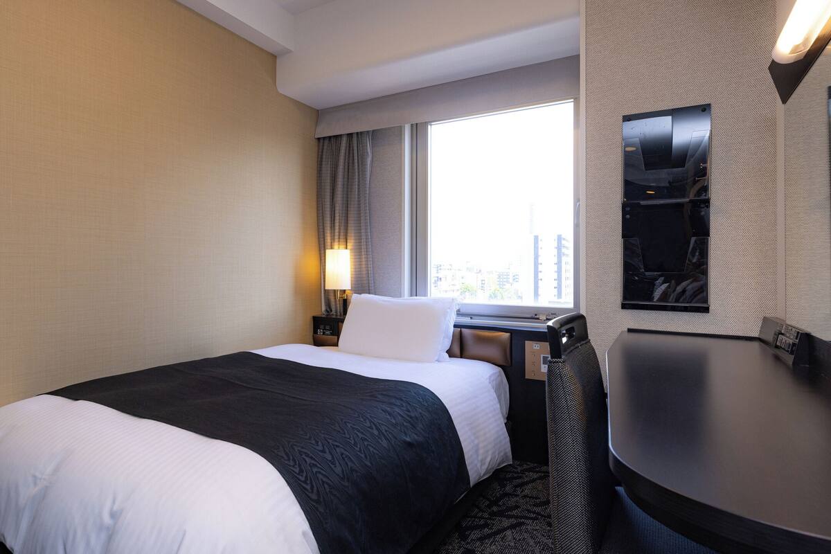Een hotelkamer met een bed, een bureau, een televisie en een raam met gordijnen.
