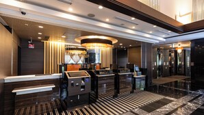A modern hotel lobby with a reception desk, self-service kiosks, and a chandelier.